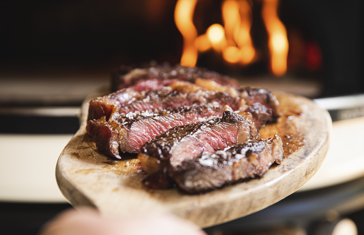 steak cut up on a board in front of a pizza oven