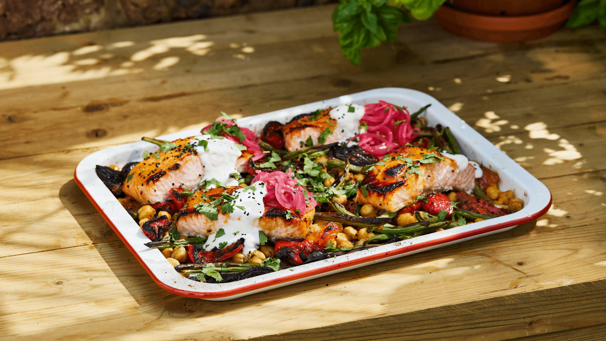 Salmon Traybake on a wood countertop with a plant in the background. recipe poster image